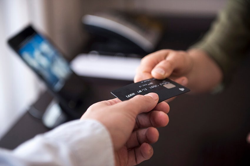 shopper handing over credit card with screen and phone in the background