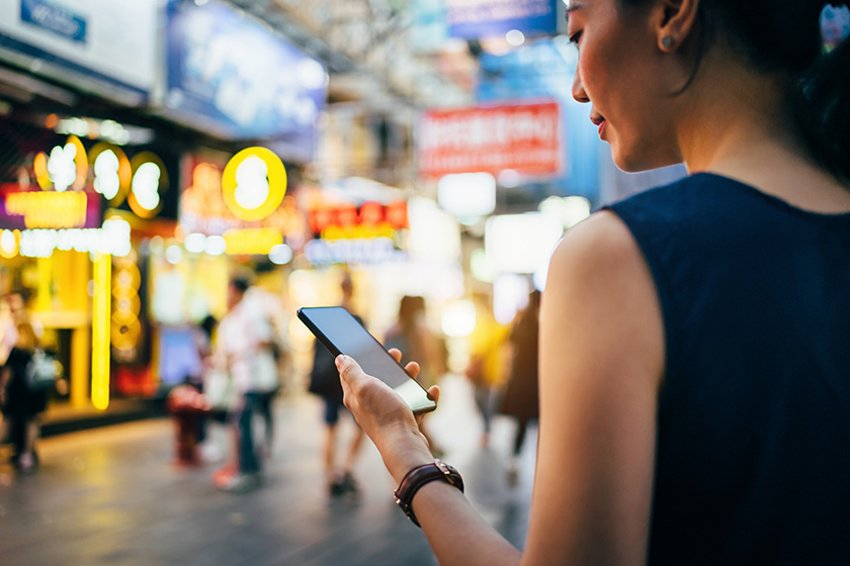 Femme tenant un téléphone devant des boutiques