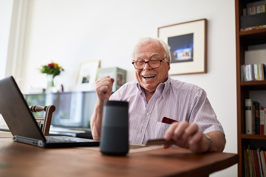 Personne âgée faisant des achats en ligne à l'aide d'une carte de crédit, d'un ordinateur portable et d'une enceinte connectée.