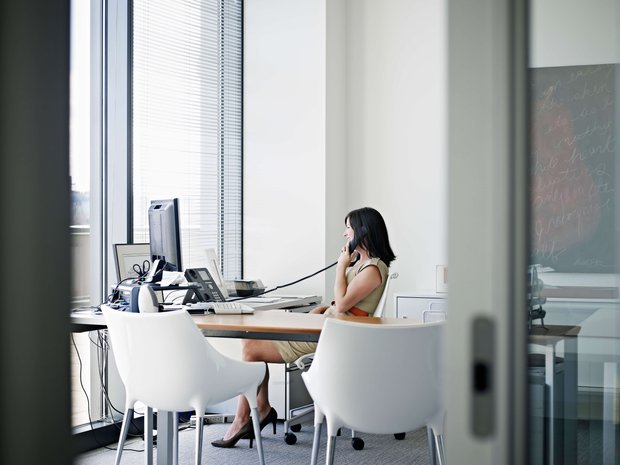 VoIP Tech Businesswoman sitting at desk in office talking on phone smiling